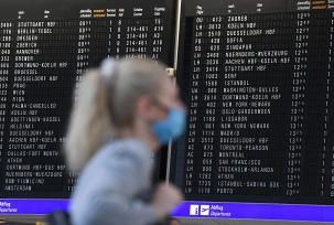 Eine Frau, die einen Mundschutz trägt, steht im Terminal 1 des Frankfurter Flughafens in der Abflughalle vor einer Anzeigetafel, © dpa/Arne Dedert