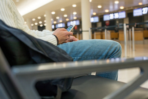 Ein Passagier sitzt mit dem Handy in der Hand auf einer Bank im Flughafen., © DPA/Christin Klose