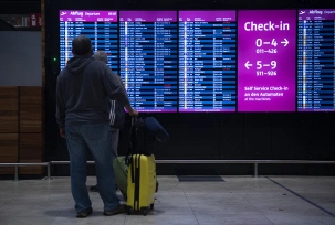 Berlin: Zwei Passagiere stehen am Flughafen BER vor einer Informationstafel., © DPA/Paul Zinken