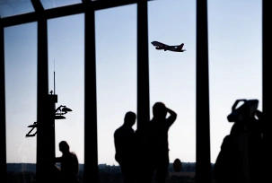Passagiere beobachten am Flughafen ein startendes Flugzeug in der Dämmerung., © DPA/Christoph Soeder