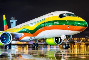 Ein Airbus A220 von Air Baltic mit Sonderbemalung der litauischen Flagge steht bei Nacht auf dem Vorfeld., © AirTeamImages.com/Yochai
