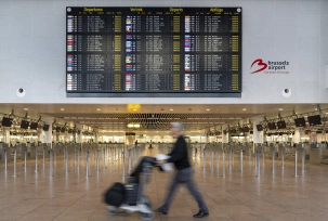 Infotafel zeigt die gestrichenen Flüge aufgrund eines Streiks am Brüsseler Flughafen an, während ein Reisender einen Gepäckwagen im Terminal schiebt., © DPA/Marius Burgelman