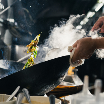 Koch bereitet Gemüse im Wok über offener Flamme zu, © Adobe Stock/U2M Brand