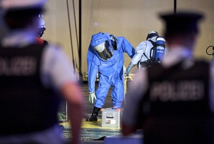 Ein Mitglied der Feuerwehr in einem Chemikalienschutzanzug wird von einem Kollegen vor dem Terminal 1 am Flughafen BER dekontaminiert., © DPA/Michael Ukas