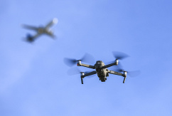 Eine Drohne fliegt vor einem startenden Flugzeug in der Nähe eines Flughafens., © DPA/Jan Woitas